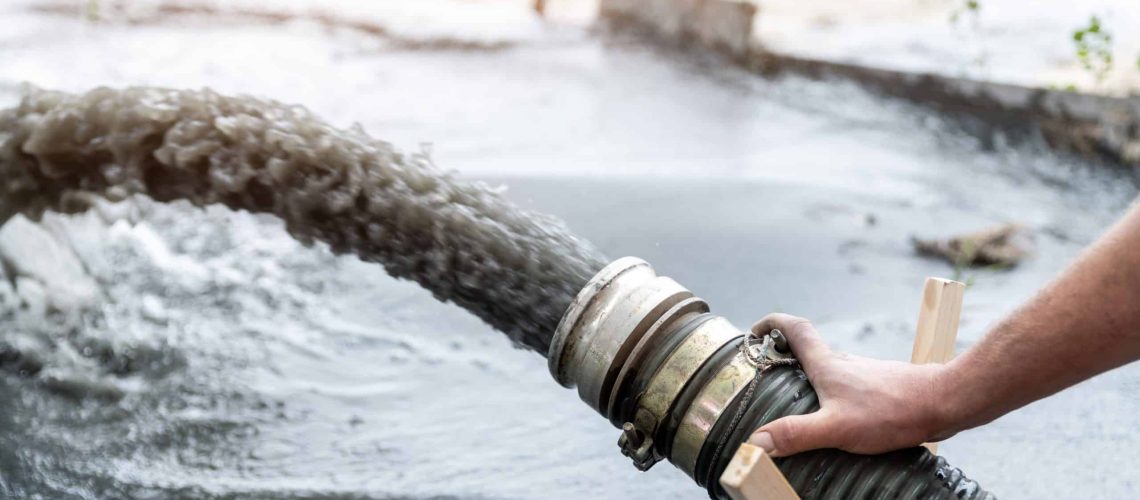 Engeneer hold pipe of power pump machine pouring mud sludge waste water with sand silt on ground. Sand-wash and coast-depeening. Septic sewage maintenance service. Industrial environment pollution.